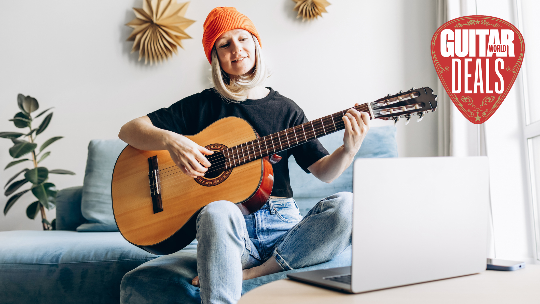 Woman wearing orange hat plays guitar in front of her laptop