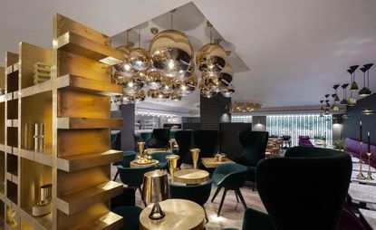 The luxurious dining room of the Tom Dixon Sandwich features a black sofa chair, gold table, and a big round golden ceiling ball