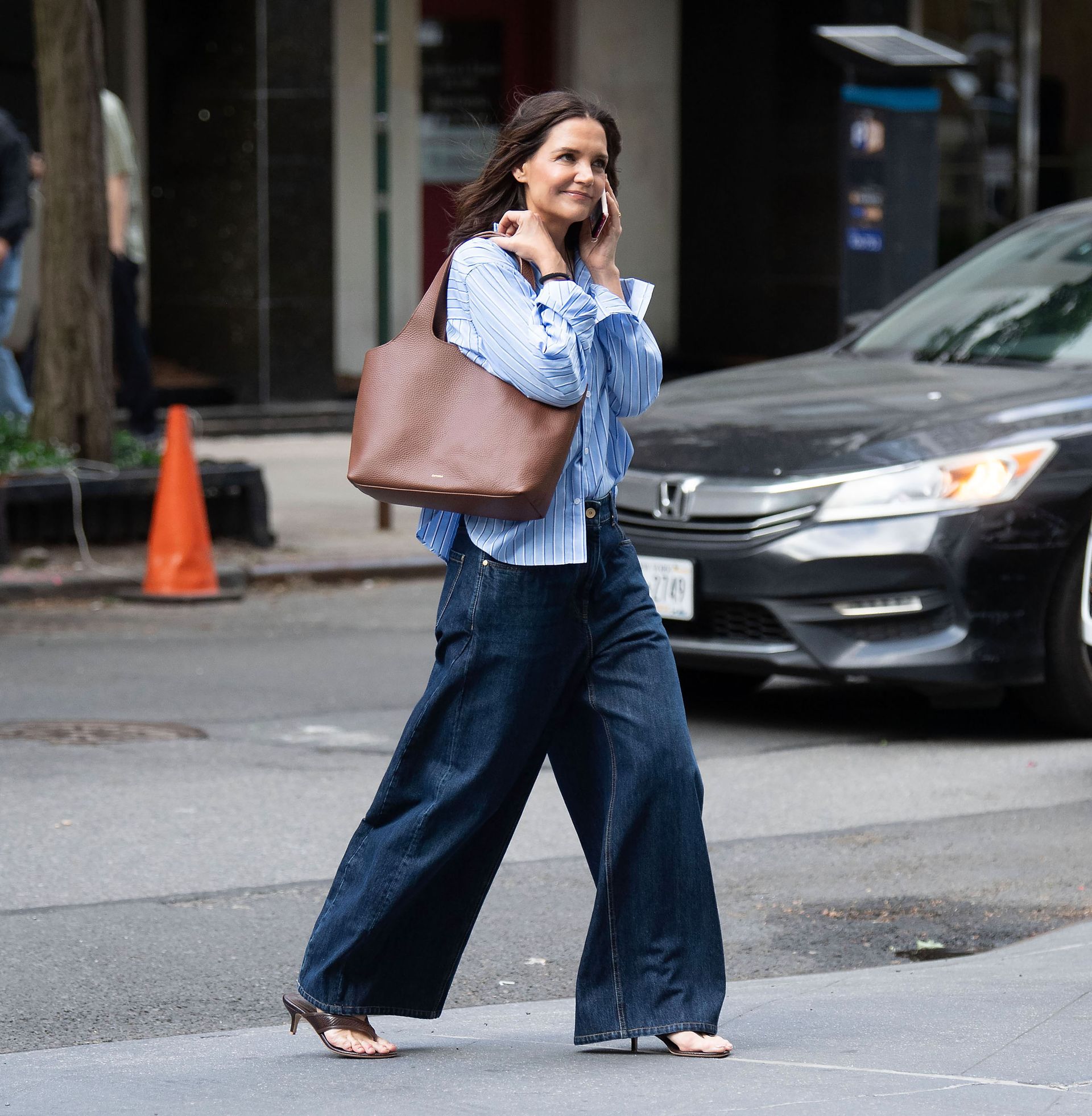 Katie Holmes wears a brown tote bag, blue stripe shirt, palazzo jeans, and heeled flip-flops.