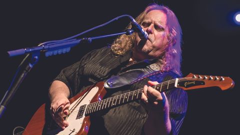 Warren Haynes singing into a microphone and playing guitar.