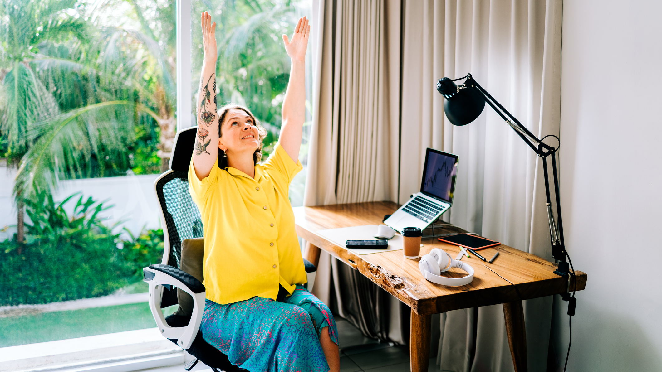 Woman sits at desk with her arms raised in the air