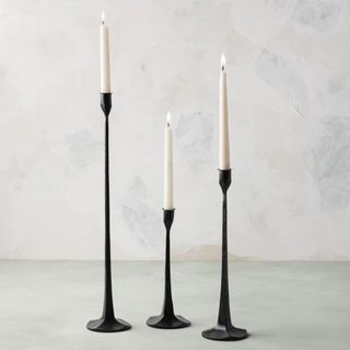 Threee Black Gatecrest candleholders, holding lit candles in a studio