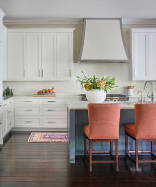 kitchen with dark wood floors, warm white cabinets and island painted blue with two red bar seats