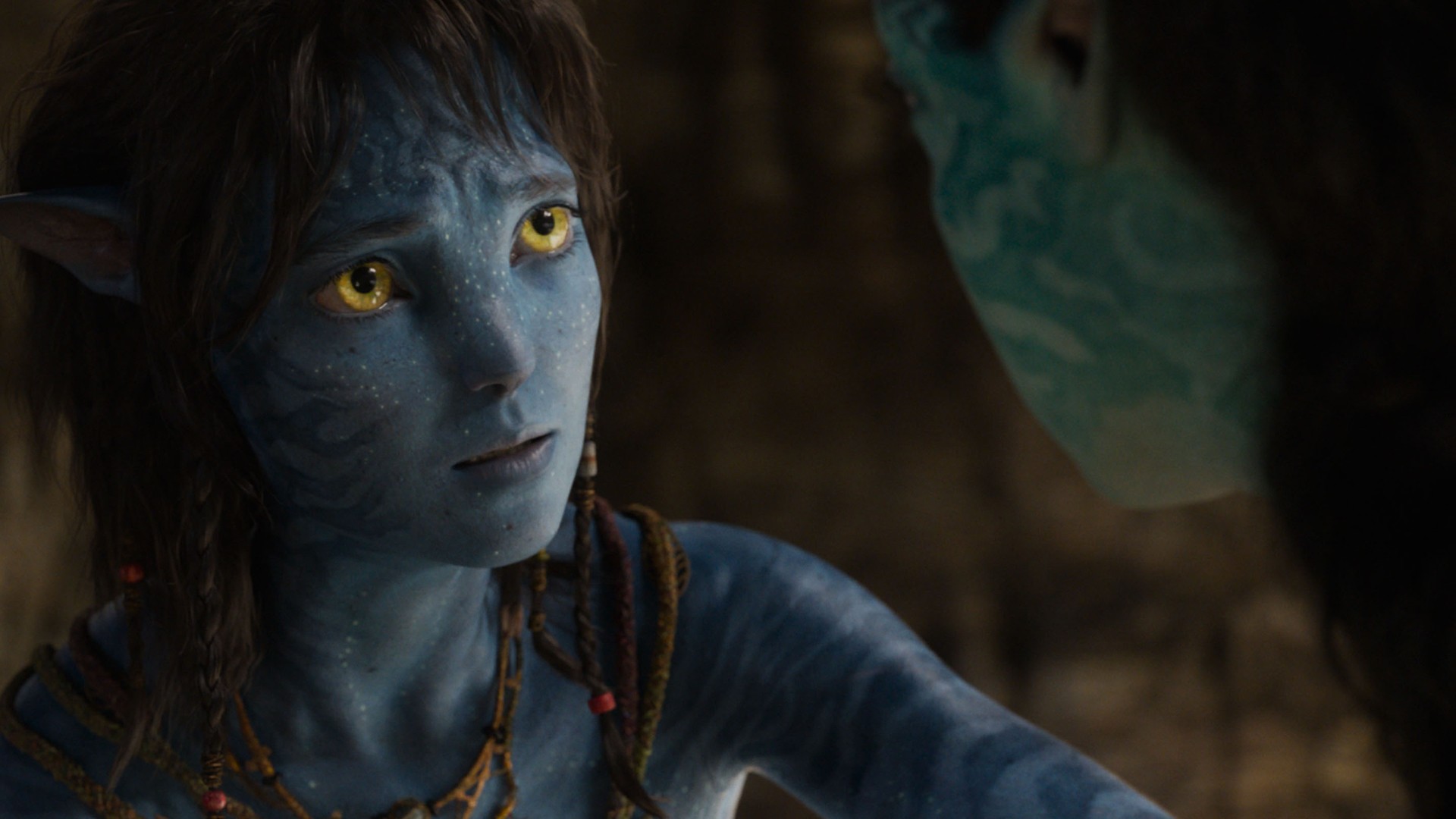 Still from the movie Avatar: Fire and Ash. A blue-skinned and yellow-eyed female Na&#039;vi is looking up at another Na&#039;vi with deep concern.