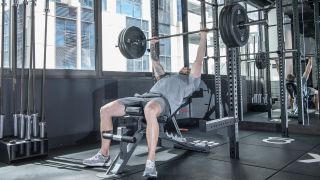 Man performs incline bench press with barbell in gym