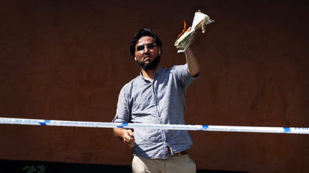 A man holding up a copy of the Koran that is on fire