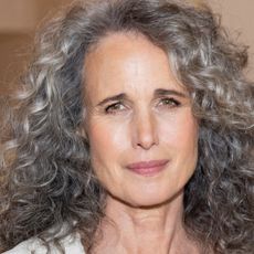 Andie MacDowell with curly hair and skin-like makeup on, posing for the camera.