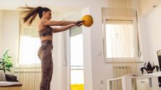 A woman performing a kettlebell swing in her living room