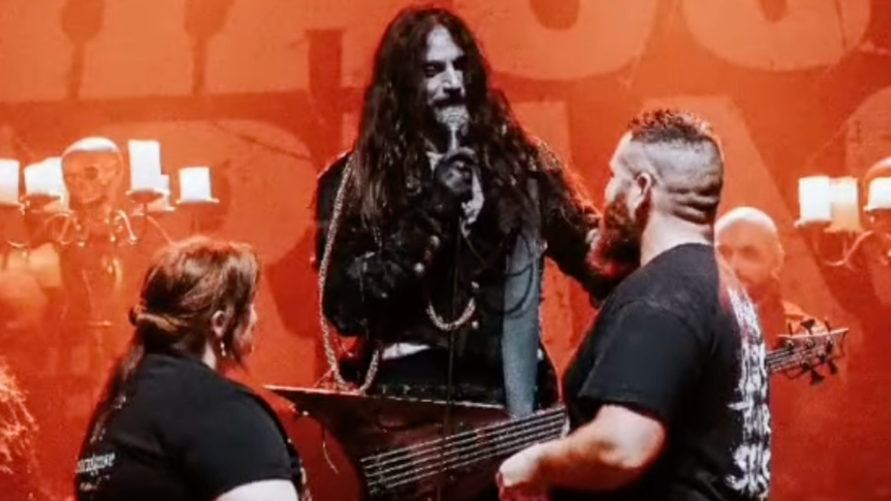 The singer/bassist of Fleshgod Apocalypse standing onstage, with a couple holding hands in front of him