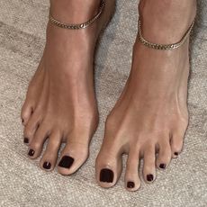 A close up of feet wearing gold anklets, with a dark red nail polish colour painted on the toes