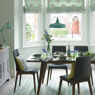 A green dining room with patterned wallpaper and blinds