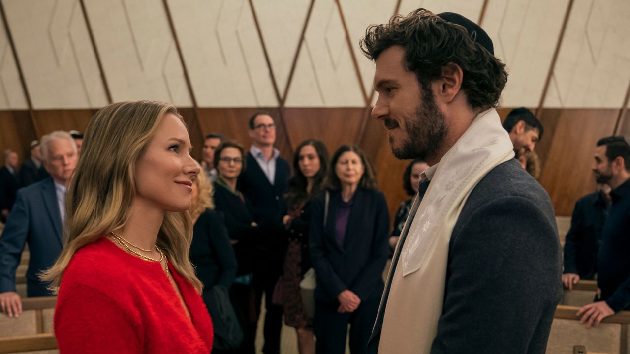 Kristen Bell as Joanne and Adam Brody as Noah, standing in front of congregants at a synagogue, in episode 102 of Nobody Wants This.