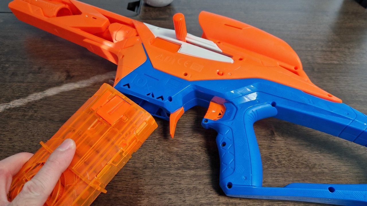A hand holding the Nerf N-Series Pinpoint clip as the blaster sits on a wooden surface