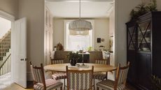 Breakfast table with bistro chairs, low pleated pendant lights, black armoire with tableware looking into the kitchen