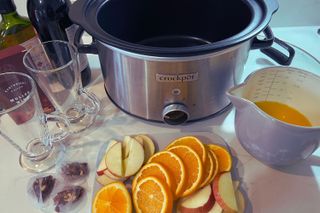 Ingredients to make mulled wine; oranges sliced, apples, jug of orange juice bottle of red wine and slow cooker