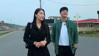 a woman and a man walk down an empty street during daytime, in the korean show 'i am solo'
