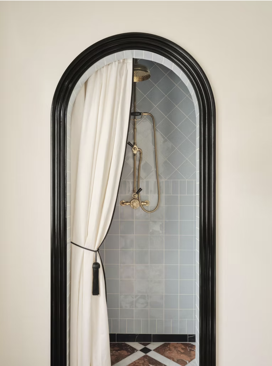 walk-in shower with arched door way and cream curtain with black tassel tieback