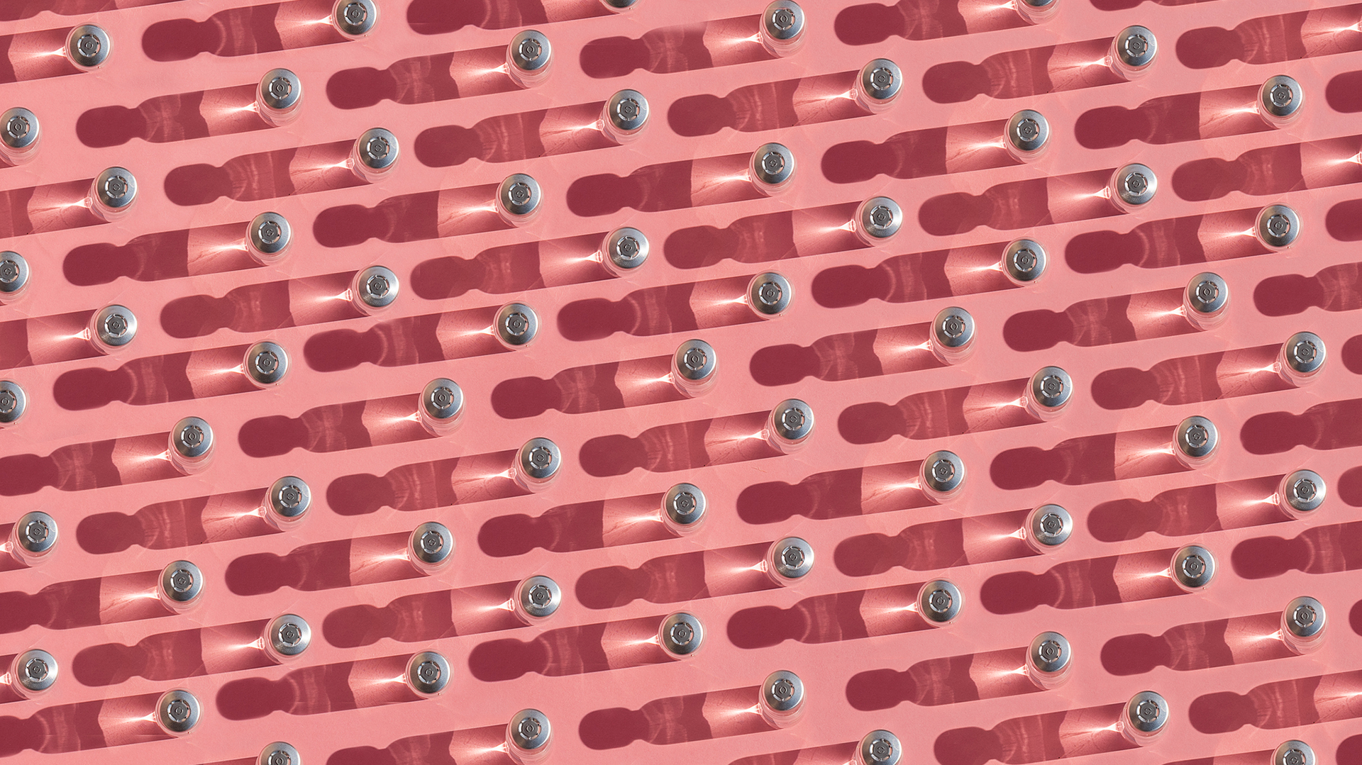 A pattern of glass bottles with light to the right of the image against a pink surface.