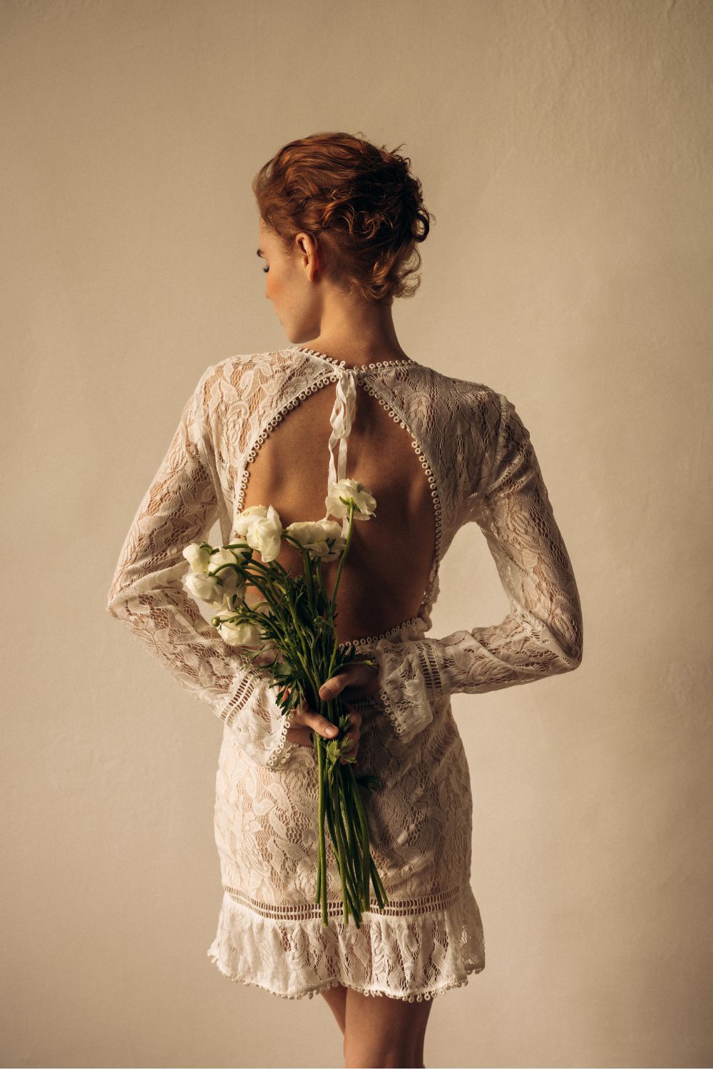 a model facing away from the camera in a wedding dress holding a bouquet of ranunculus - wedding beauty timeline