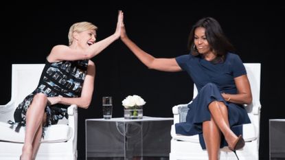 Charlize Theron and Michelle Obama high five across a table.