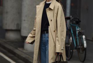 Woman wearing a tan trench coat with jeans.