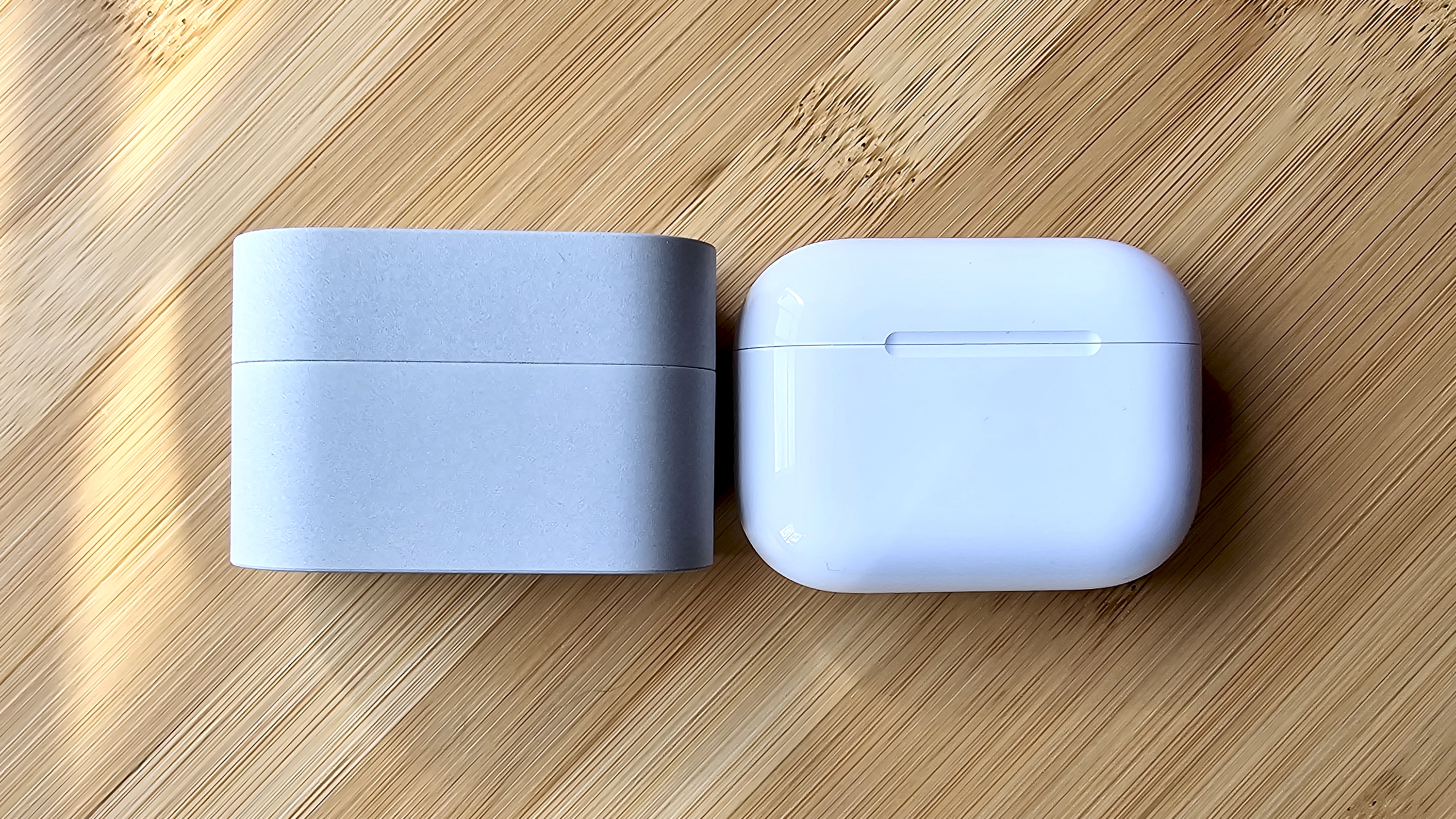 Sony WF-1000XM6 earbuds next to the Apple AirPods Pro 3, on a wooden table, in a versus-style format