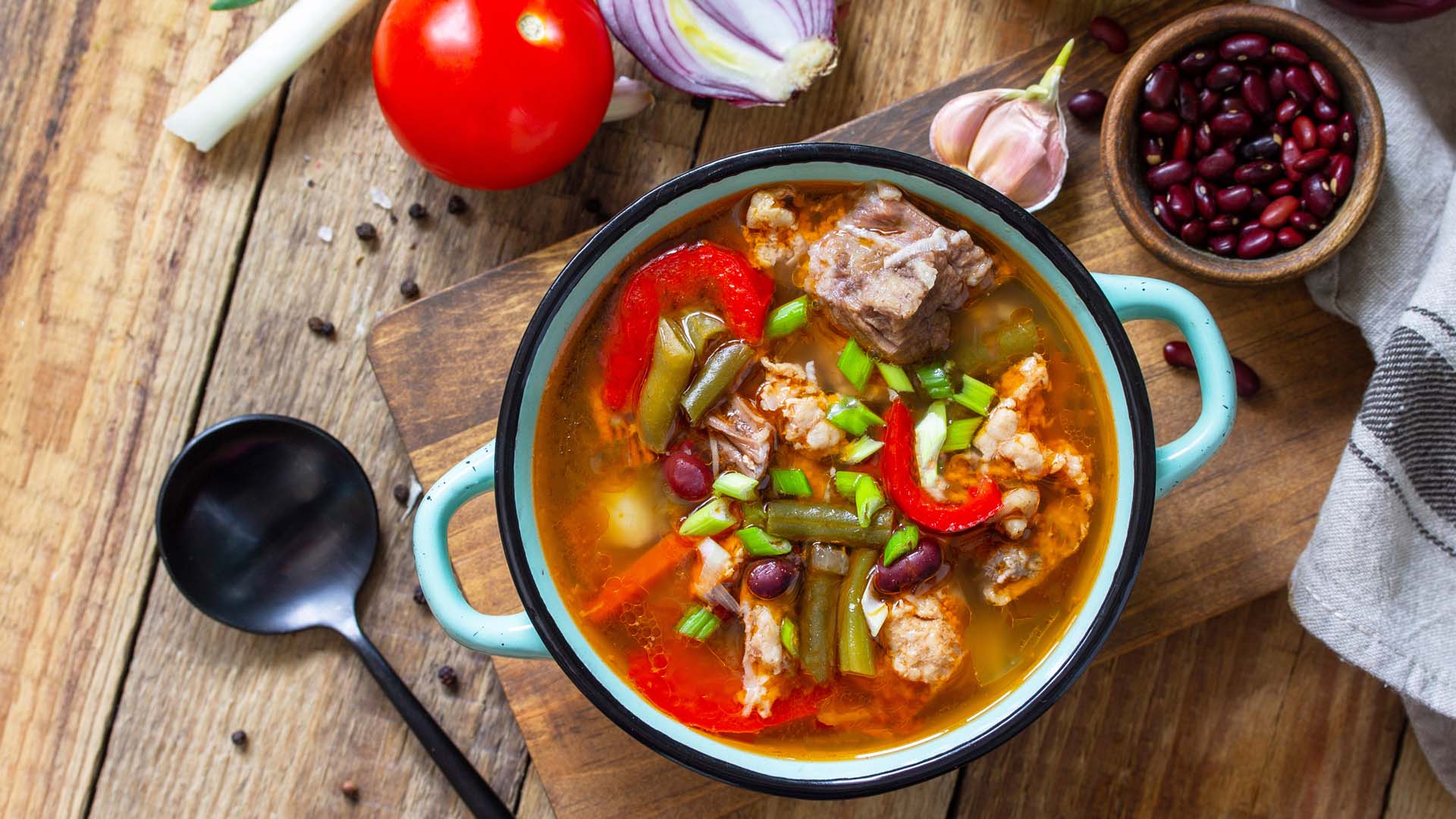 Traditional British thick soup with beef, beans and vegetables on a wooden table.