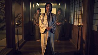Lady Mariko marche dans un couloir faiblement éclairé, entourée de ses assistants, dans la série télévisée Shogun