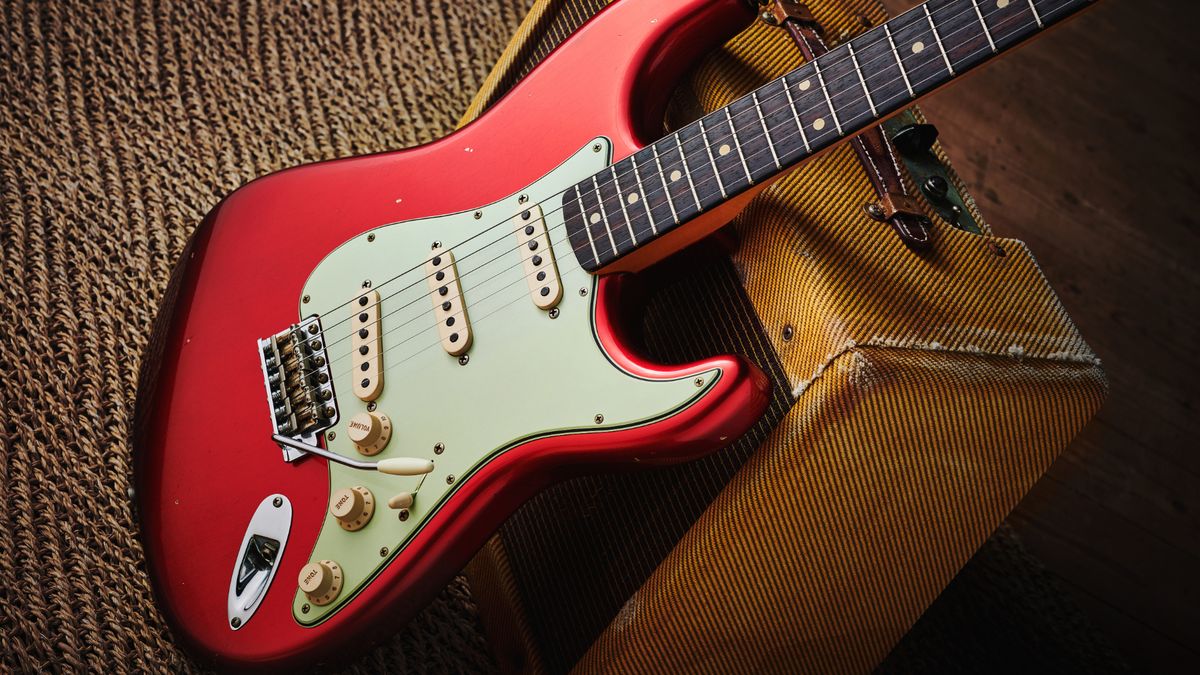 A red Fender Stratocaster leaning against a slightly worn Fender tweed amp