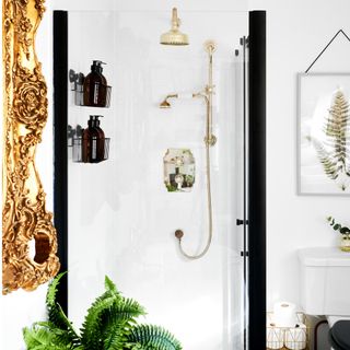 shower with white tiles, black wire baskets with bottles inside, gold shower head, gold rimmed mirror