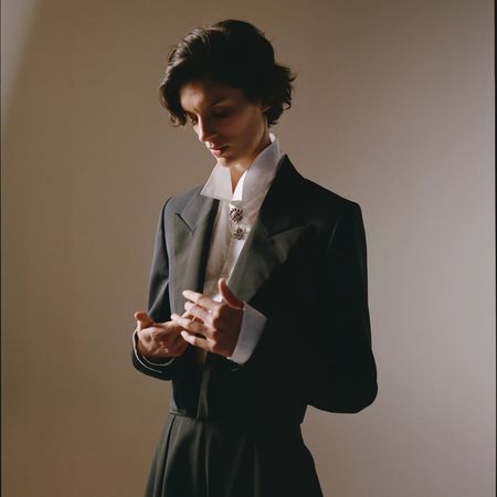 A R&oacute;he model looking down at her hands wearing a white shirt and cropped evening jacket
