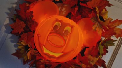 Disney Mickey Mouse Halloween Wreath with a light-up pumpkin Mickey in the middle of autumnal leaves, hanging on a white door
