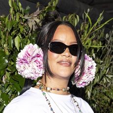Rihanna wearing pink earmuffs, a white t-shirt, blue jeans, a white scarf, and pink satin heels