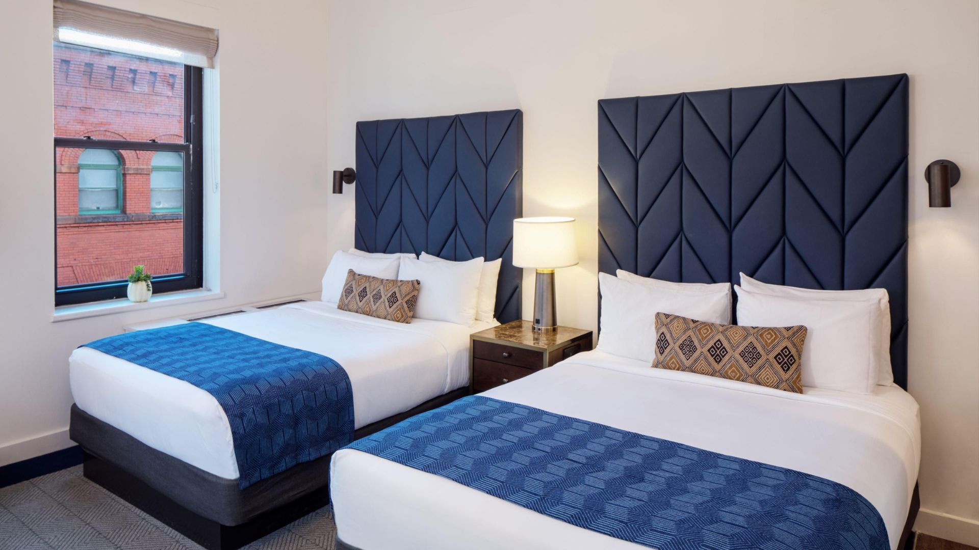 A Hotel Indigo room with two full size beds next to each other made up with white sheets and a blue runner