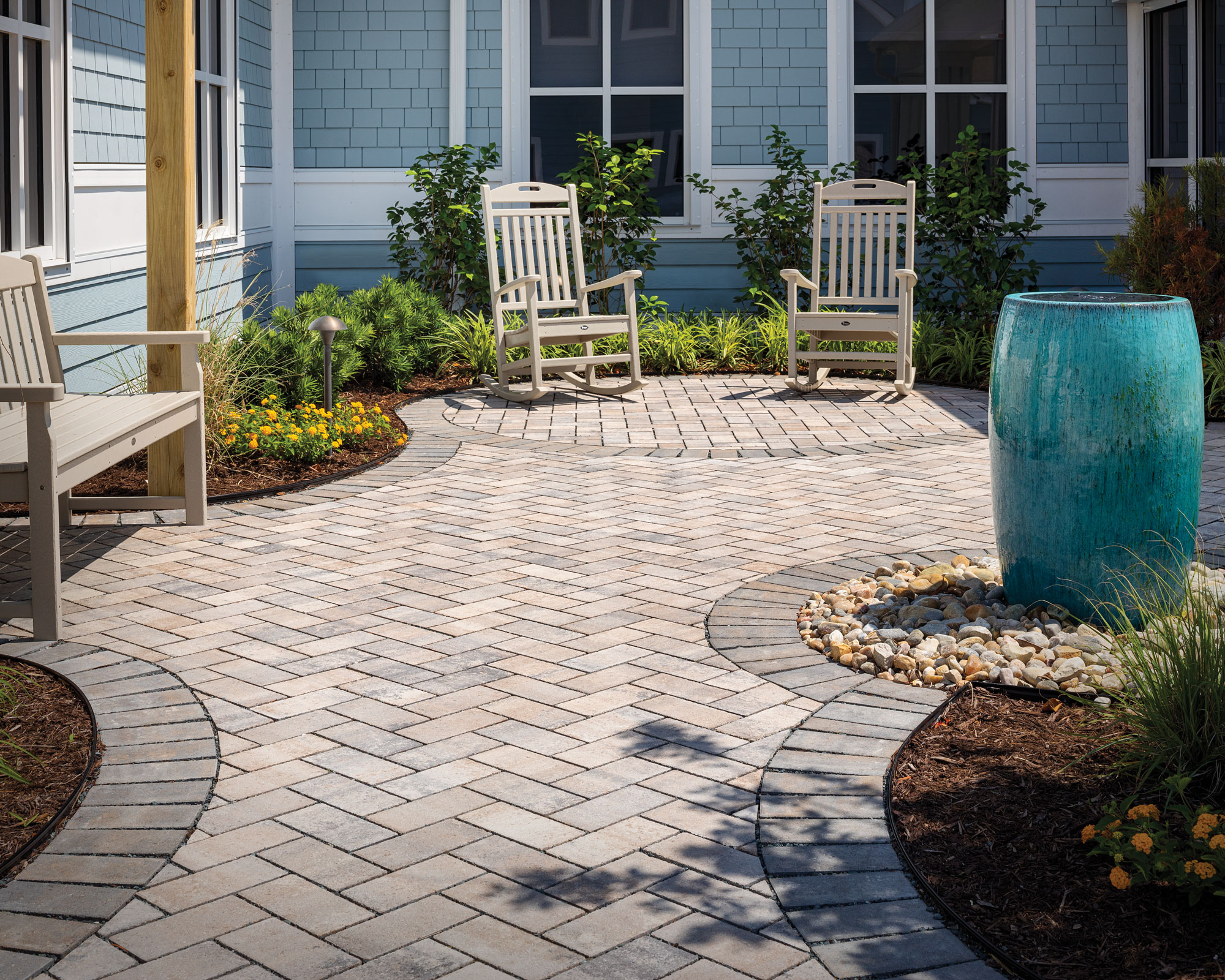 patio area with zigzag hardscaping, garden seats, flowerbeds with shrubs and ceramic planter