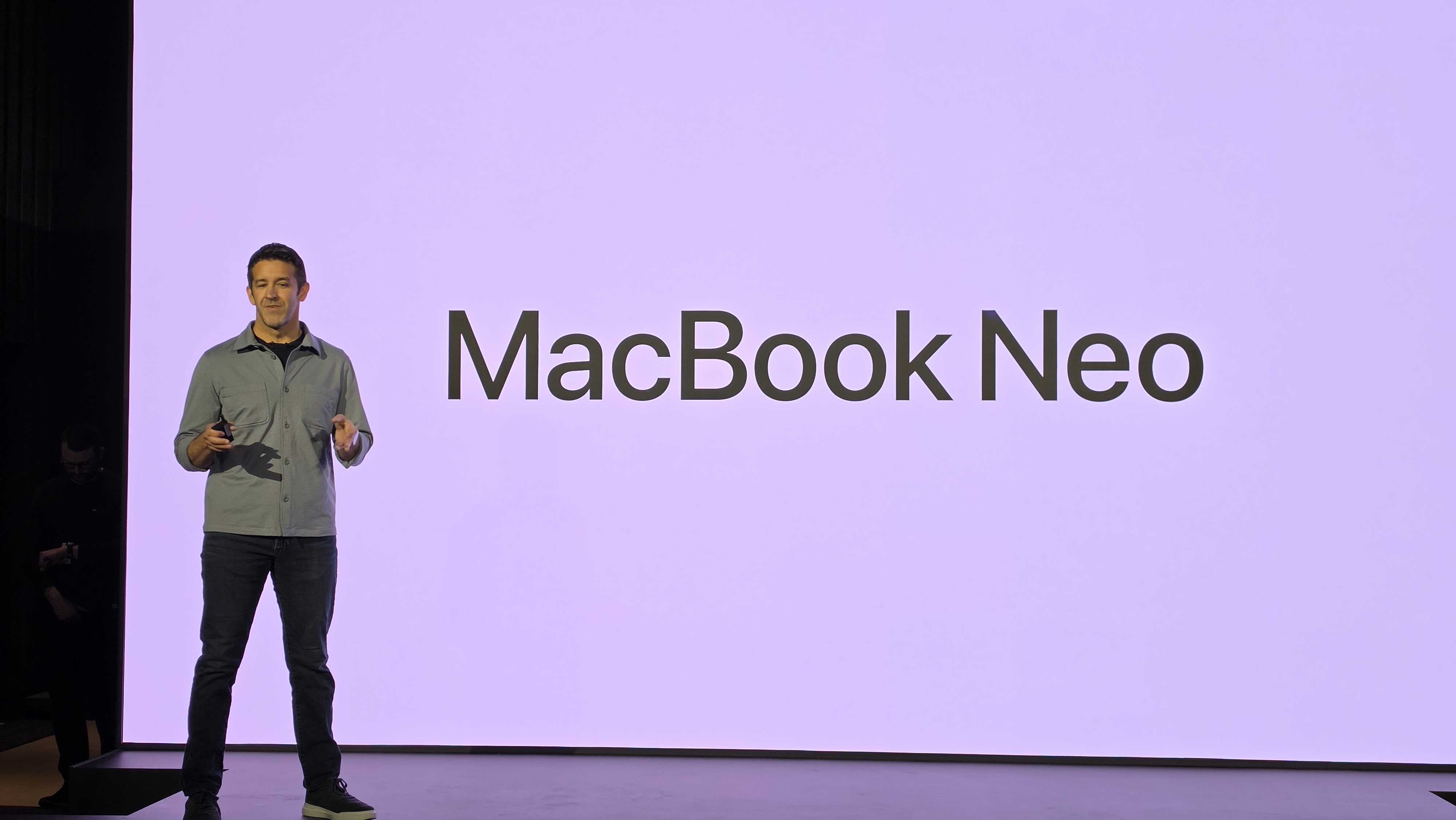 A man standing in front of a sign saying MacBook Neo