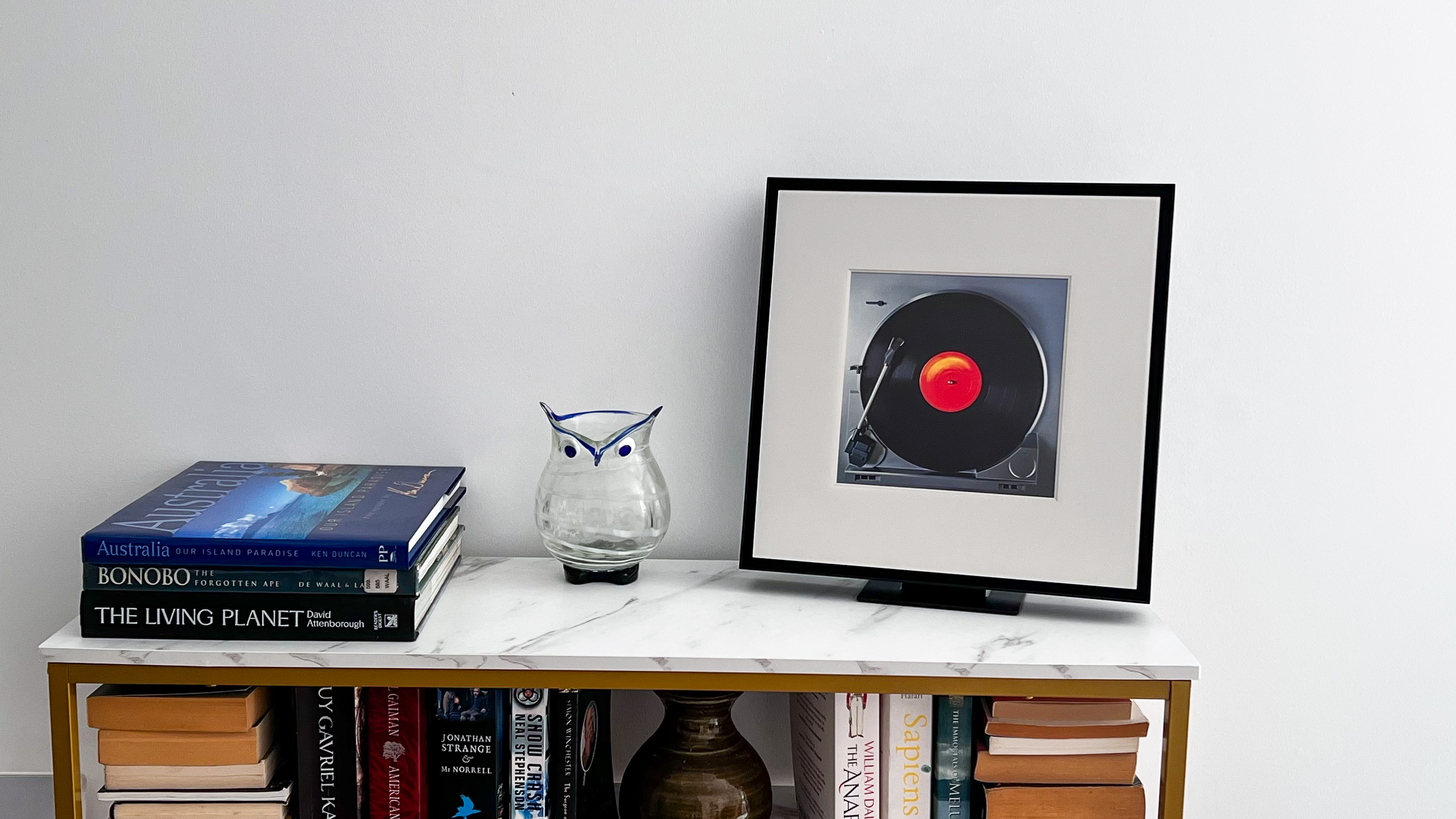 Samsung Music Frame on a table beside some books and a vase