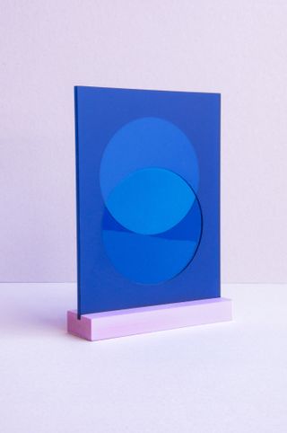 A blue slat of glass with two overlapping circles in the middle. The glass is standing portrait in a pink base // Studio Rens