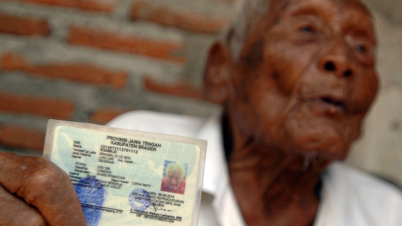 An older man holds up his ID card to the camera