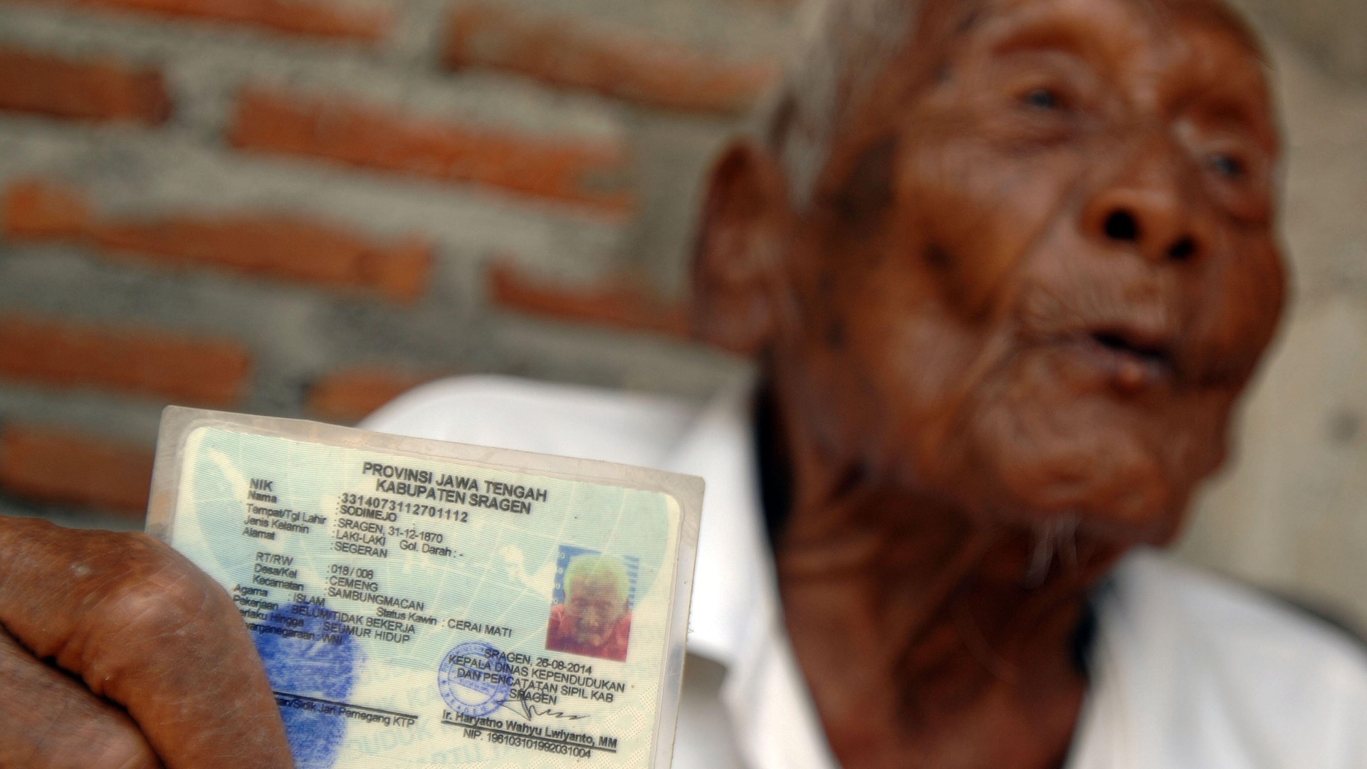 An older man holds up his ID card to the camera