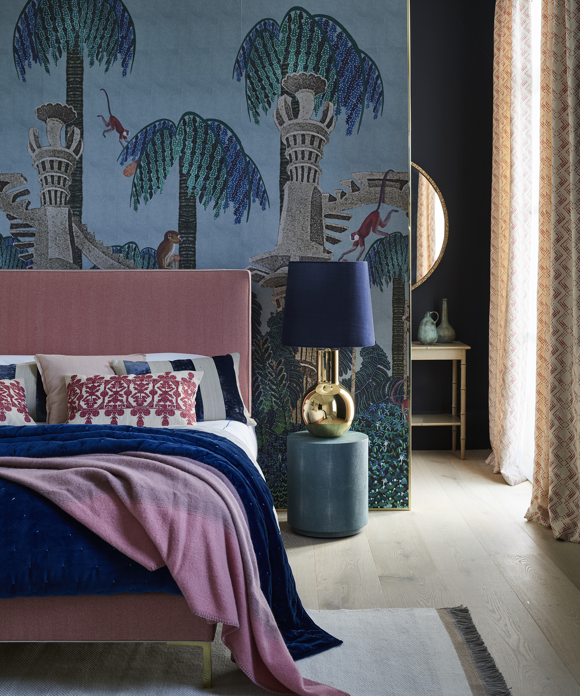 A pink bed in front of a wallpapered wall containing monkeys and trees