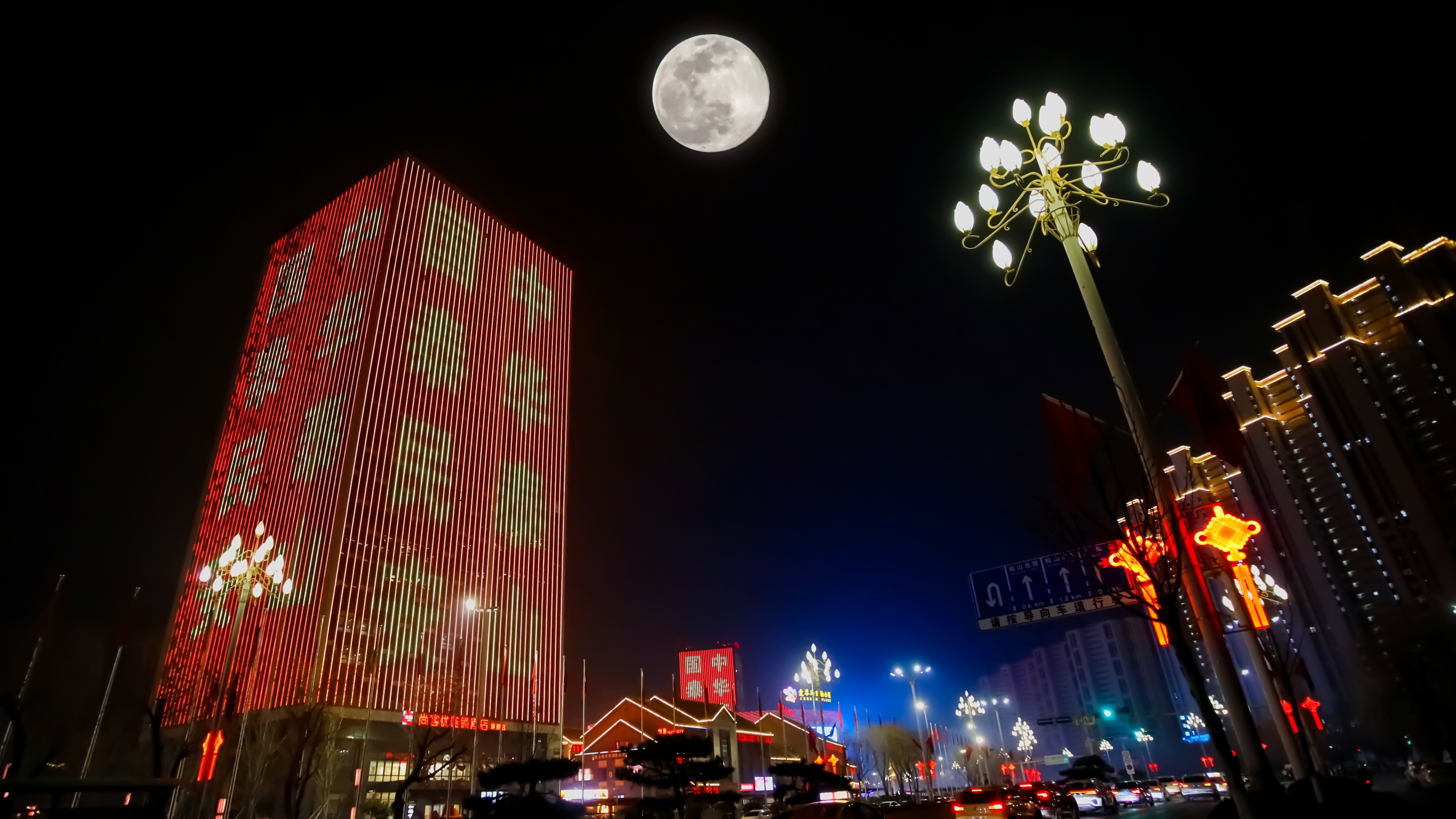 full moon over colorful buildings in china, including one building draped as a lantern in chinese characters