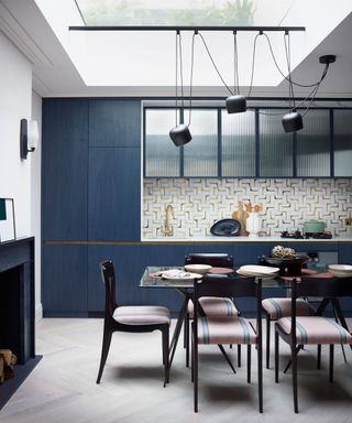 Modern kitchen with dining table, blue cabinetry, marble splashbacks, low hanging pendant lights