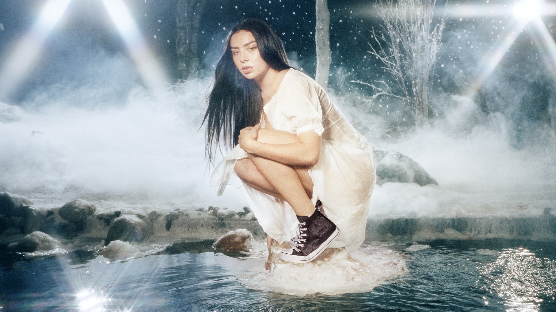 Charli XCX wears white dress and black converse while squatting and posing