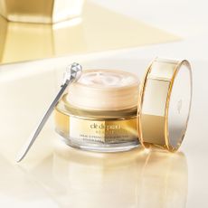 Golden Cle de peau Beaute Eye Contour Cream Supreme on white gold background with silver beauty applicator