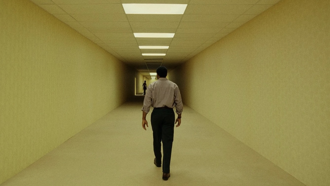 Central character from Backrooms movie walks down dimly lit corridor