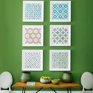Green wall with graphic framed artwork above wooden table