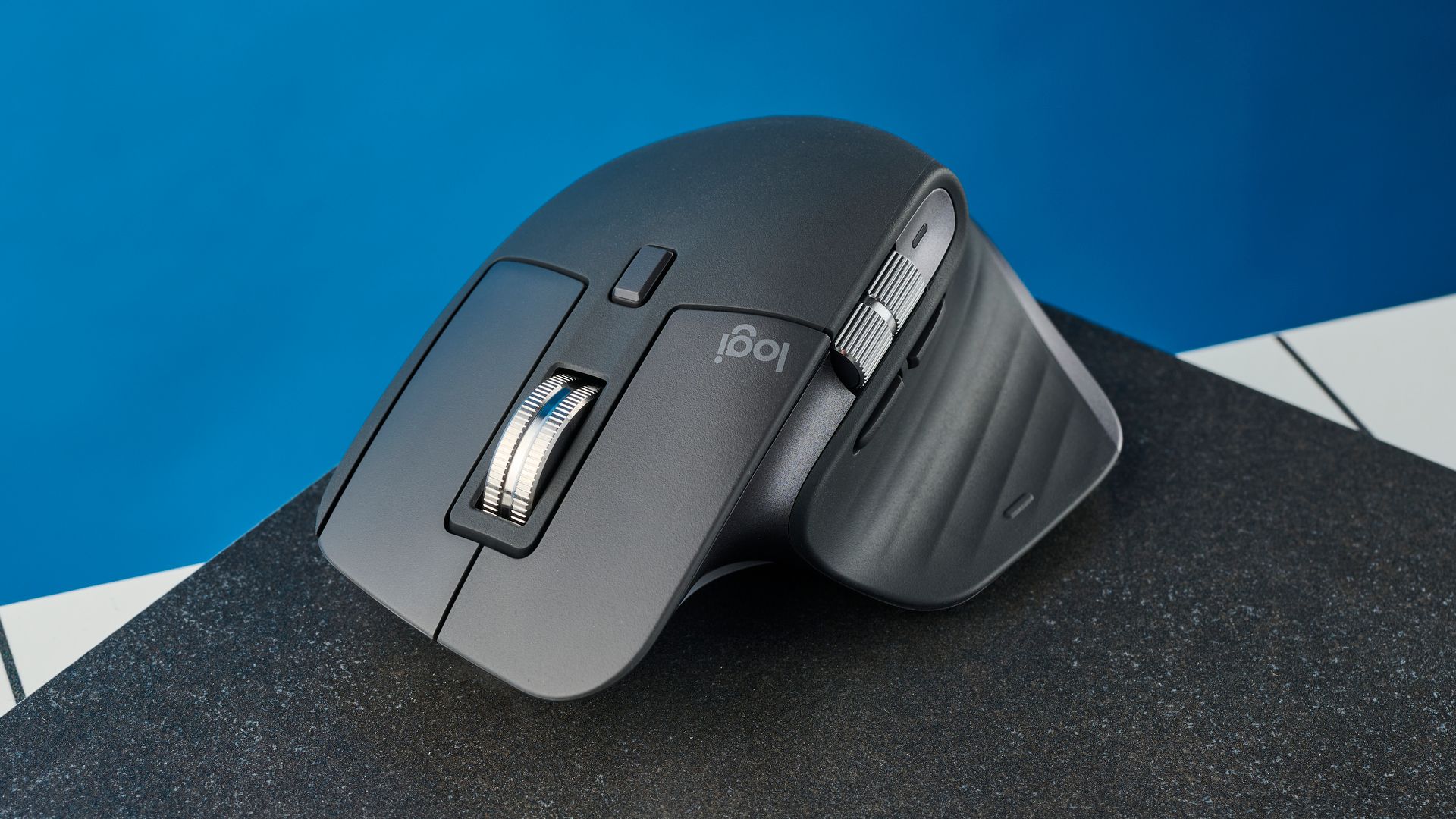 A sleek black ergonomic computer mouse with a vertical design, featuring a silver scroll wheel, rests on a textured surface in front of a blue background.