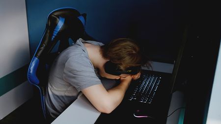Man upset at gaming PC, resting head on arms