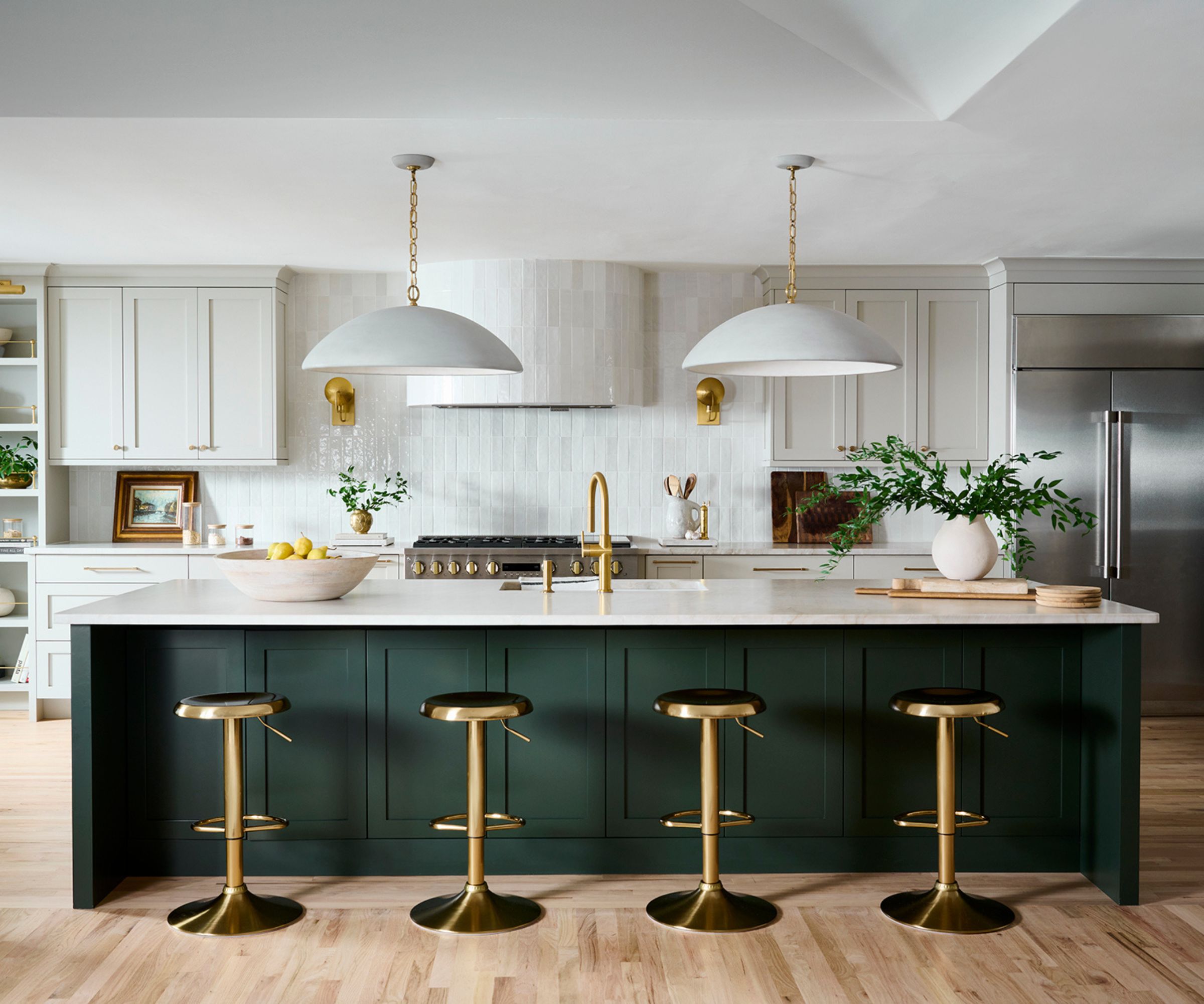 A large kitchen with white cabinets, a dark green island, and a white zellige tile backsplash that continues into a curved range hood